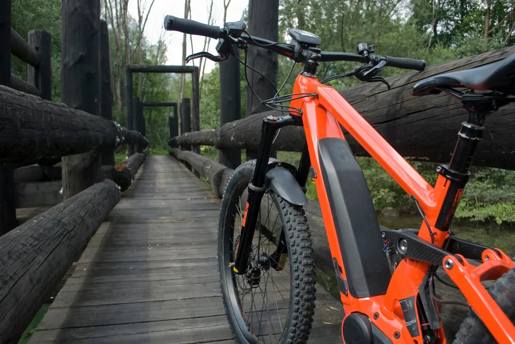 VTT électrique rouge posé contre la barrière d'un pont en bois dans une forêt.