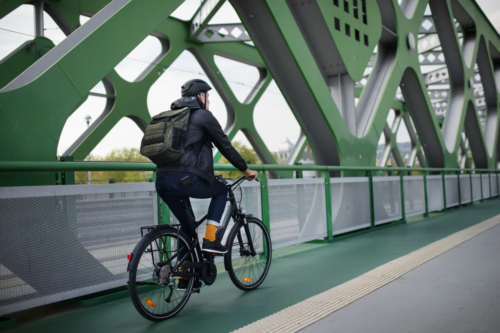 Homme sur un vélo de ville qui roule sur un pont en métal vert.