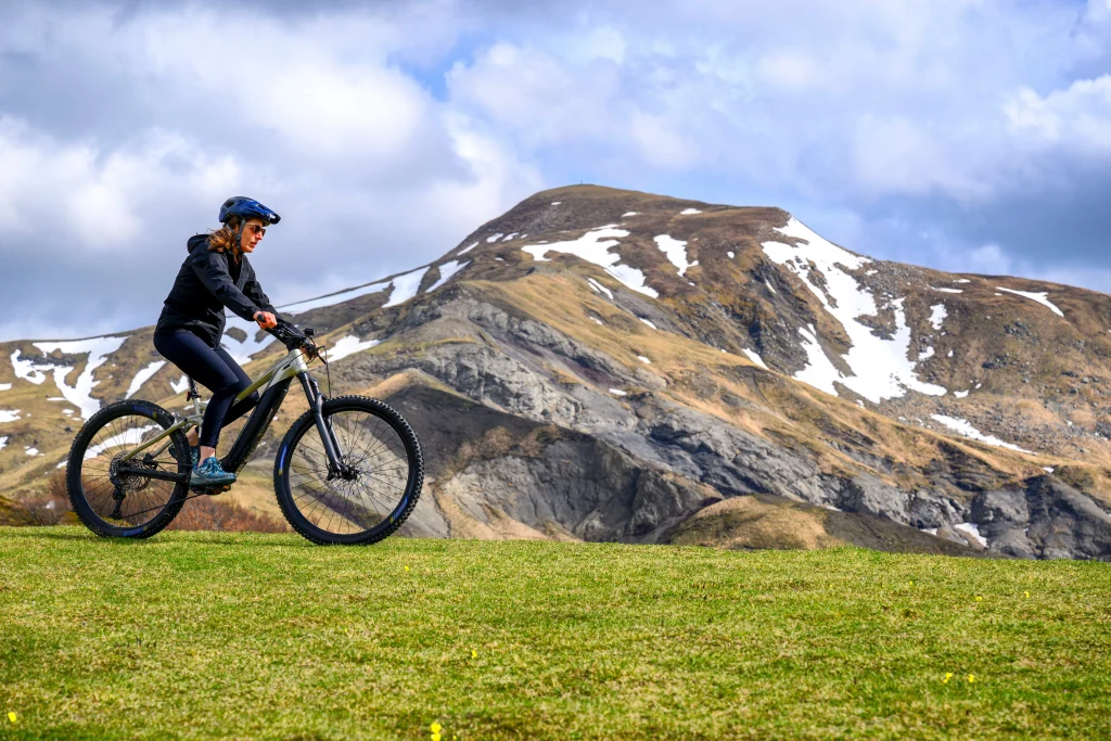 Femme qui roule dans l'herbe avec un VTT en montagne.